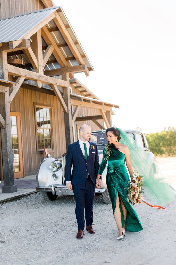 Bride in velvet green dress and her groom walking away from their wedding venue, Weston Timber Barn Farm.