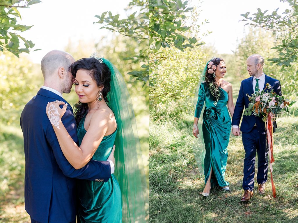 Bride with green veil embracing her groom in a navy suit in the gardens around Weston Timber Barn Farm.