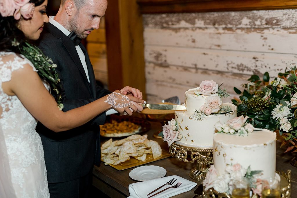 Newlyweds cutting their white wedding cake with pink roses at their reception. 