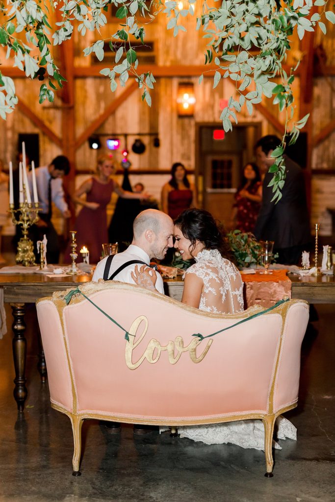 Bride and groom sharing a private moment of quiet during their busy reception while sitting on a pink couch. 