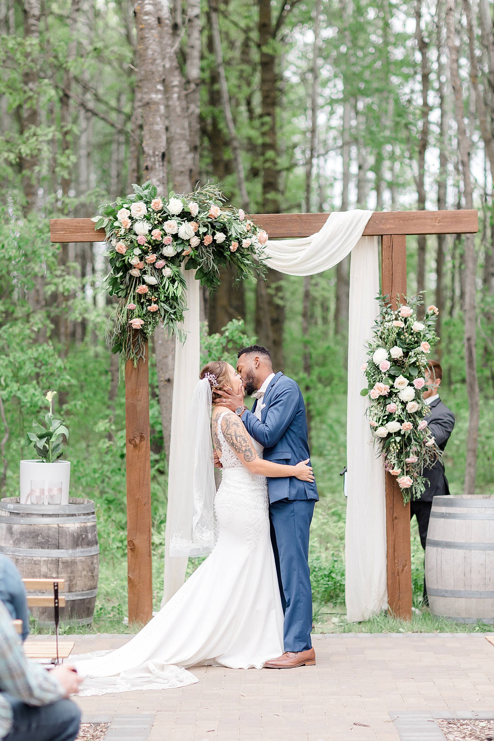 Newlyweds sharing a kiss under their wood arch & flowers 