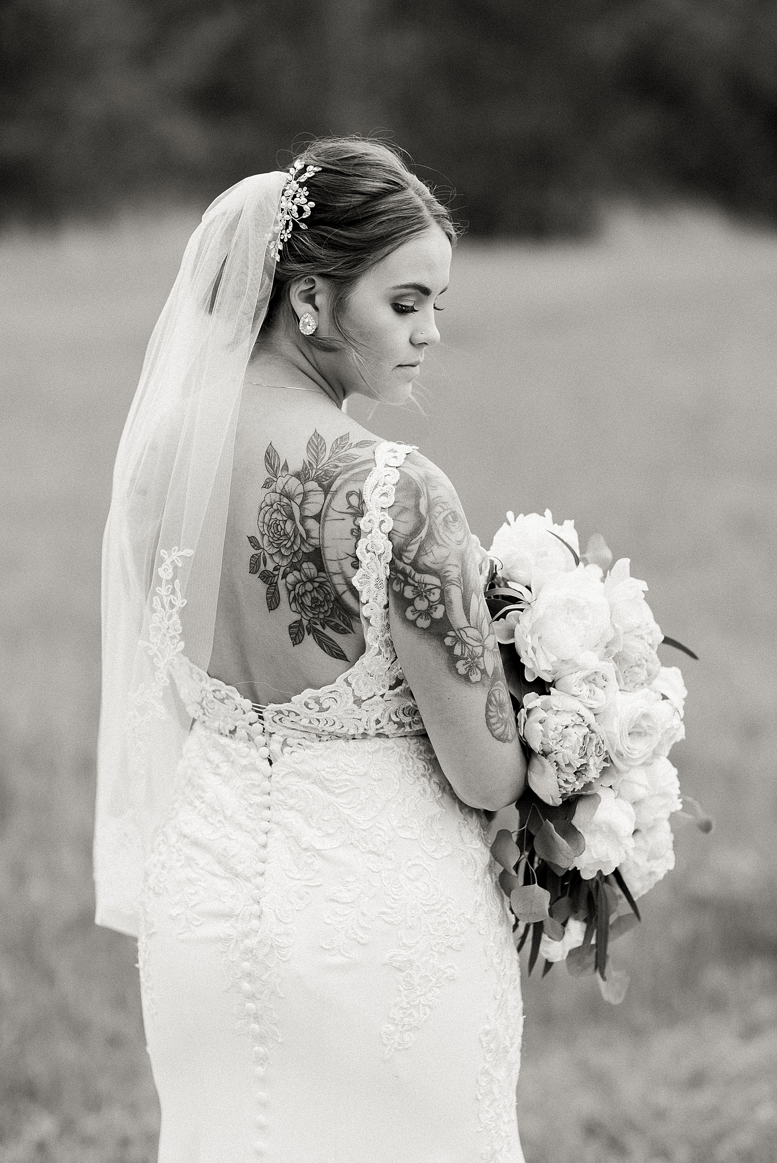 Elegant bride with tattoos looking down and holding her bouquet 