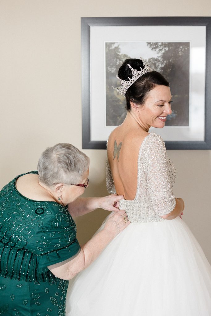 Bride getting her dress zipped up by her mother before her wedding