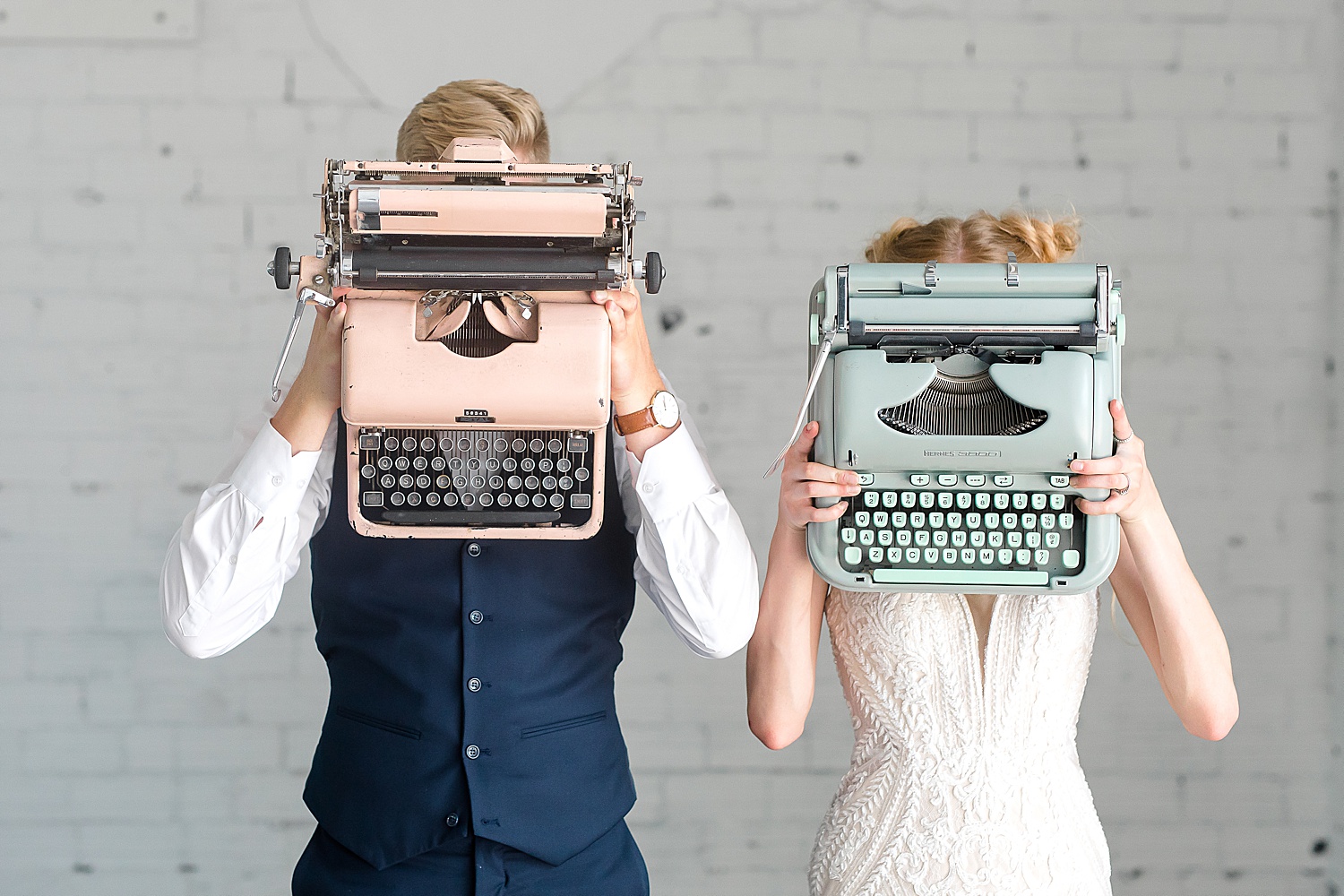 Bride and groom holding pastel typewriters in front of their faces 
