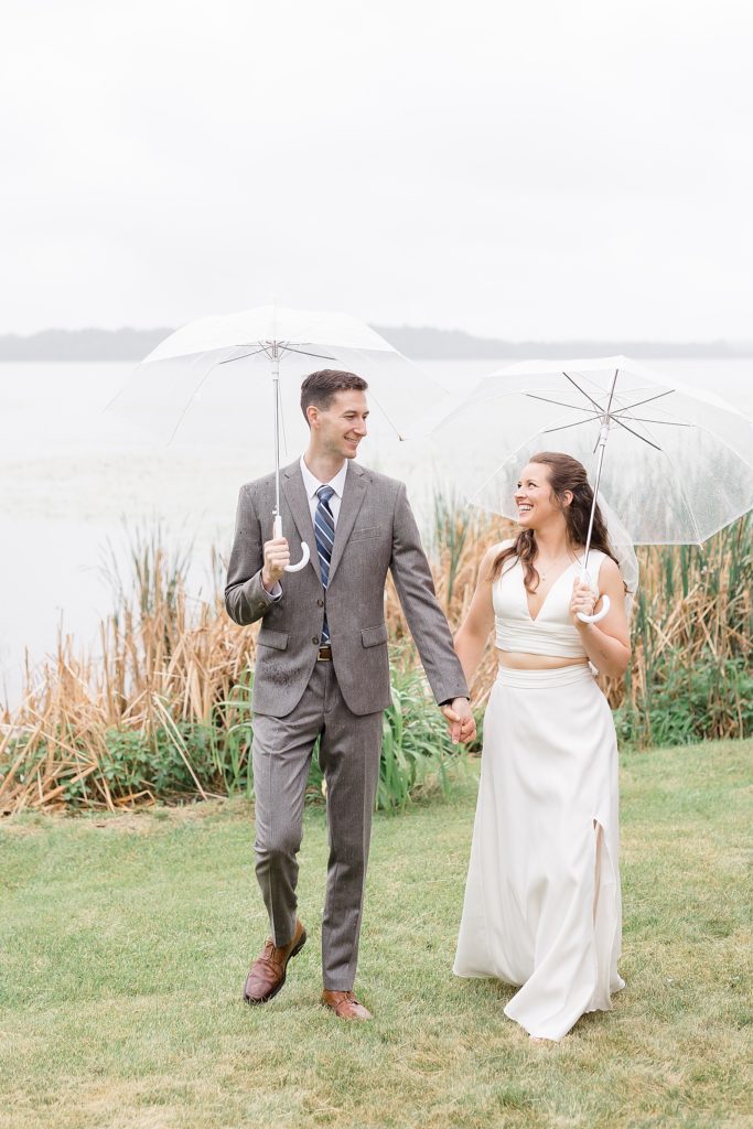 Bride and groom walking in rain under umbrellas by Fernweh & Liebe