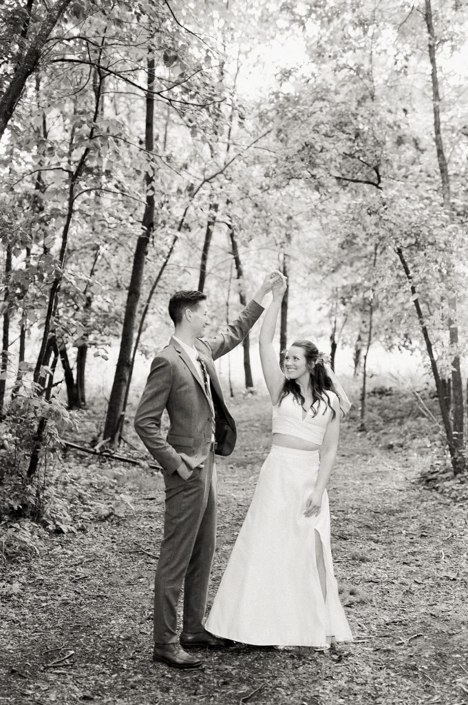 Groom twirling bride under trees at their Minnesota Lakeside Wedding